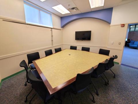 Larger meeting room with large table surrounded by chairs and TV mounted on the wall.