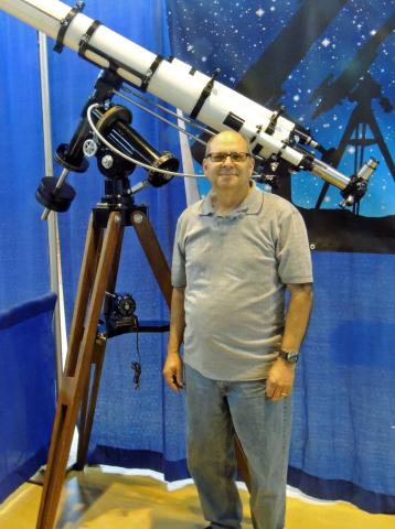 A smiling astronomer sands in front of a large telescope